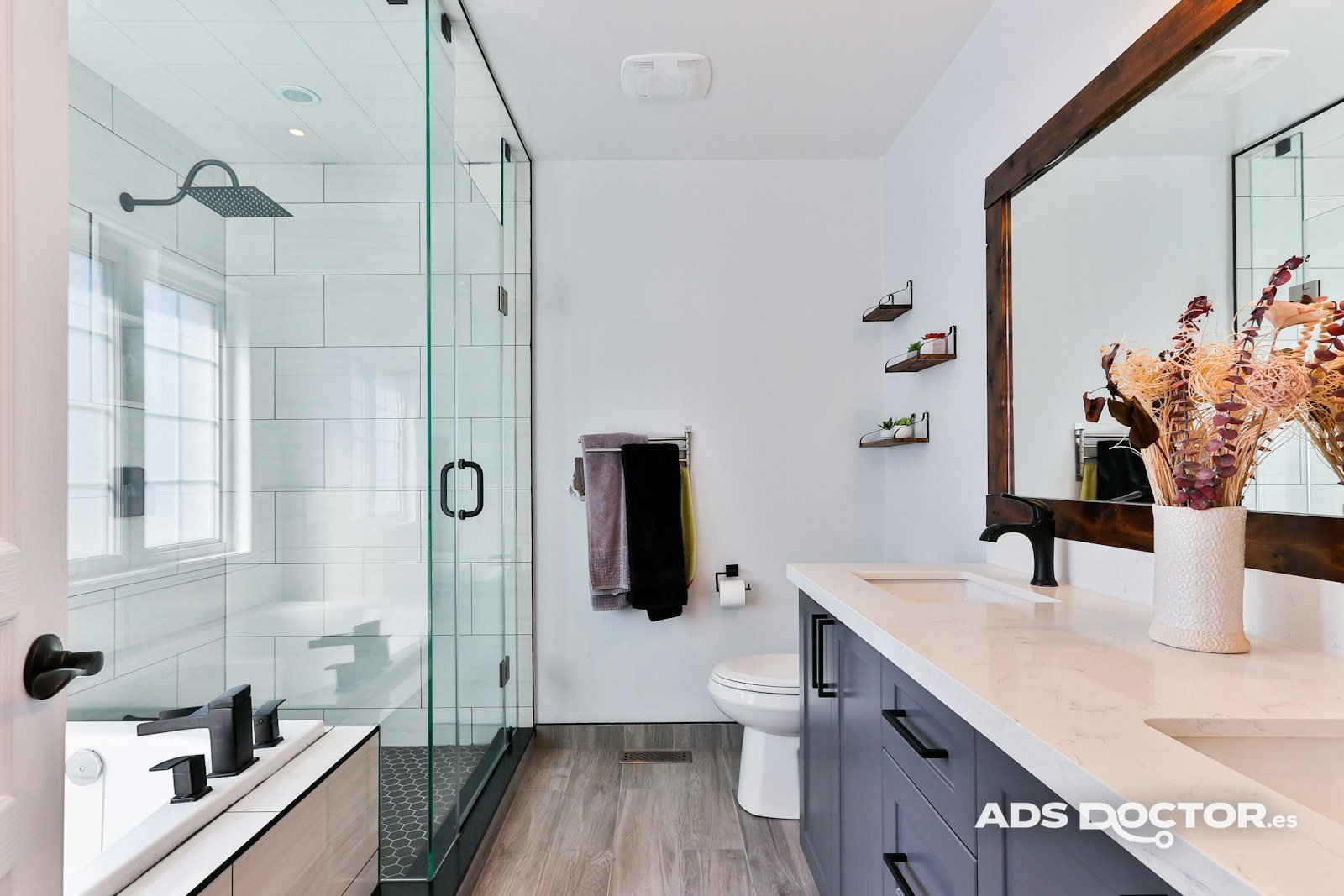Baño reformado con mampara de cristal, mueble doble y suelo de madera